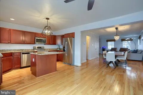 a kitchen with stainless steel appliances granite countertop a refrigerator a sink dishwasher a stove and a dining table with wooden floor