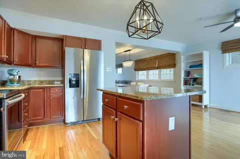 a kitchen with stainless steel appliances granite countertop a refrigerator a sink dishwasher a stove and a dining table with wooden floor