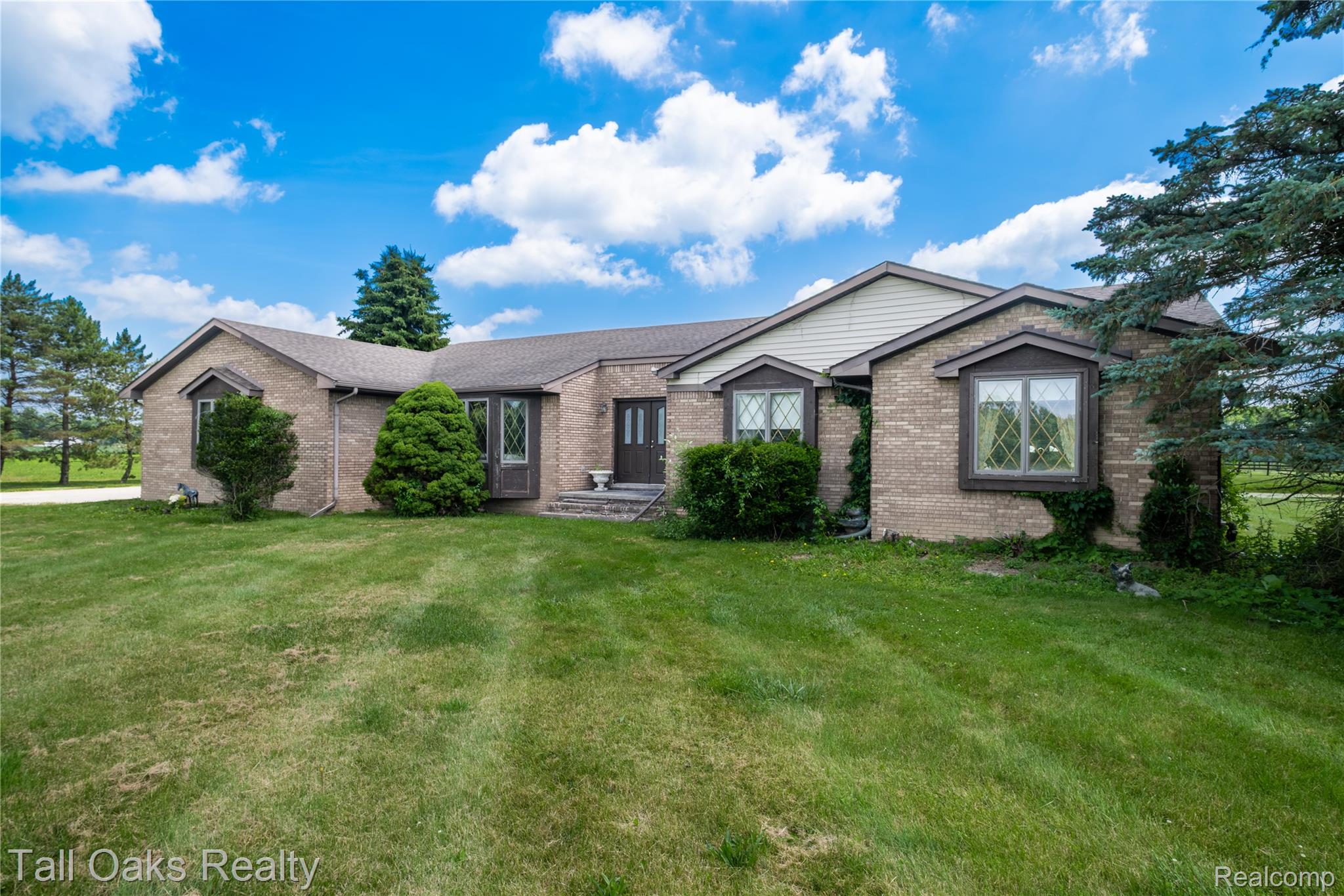 79330 Capac Road Armada, MI 48005 - Photo 19 of 42 Brick exterior featuring multiple bay windows with decorative grilles, a prominent front entry with a dark door, and a spacious front lawn