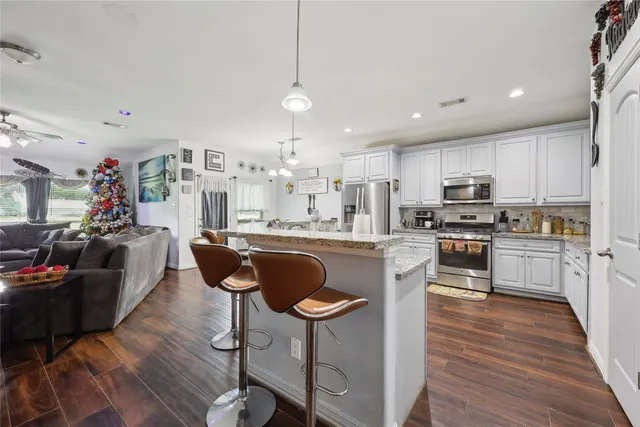 a kitchen with stainless steel appliances granite countertop a refrigerator a stove top oven a sink dishwasher a dining table and chairs with wooden floor