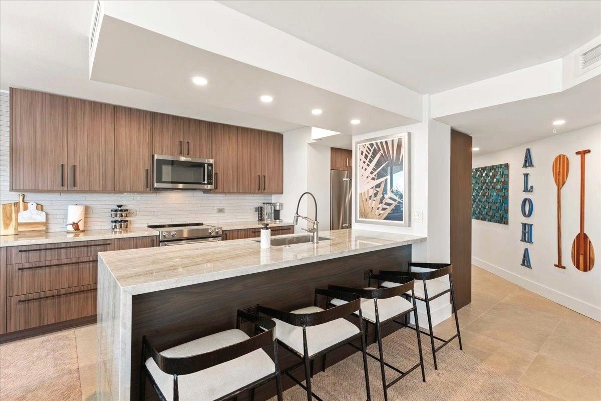 3445 Lower Honoapiilani Road, Unit 502 Lahaina, HI 96761 - Photo 23 of 50 a kitchen with stainless steel appliances granite countertop a stove a sink a microwave a dining table and chairs