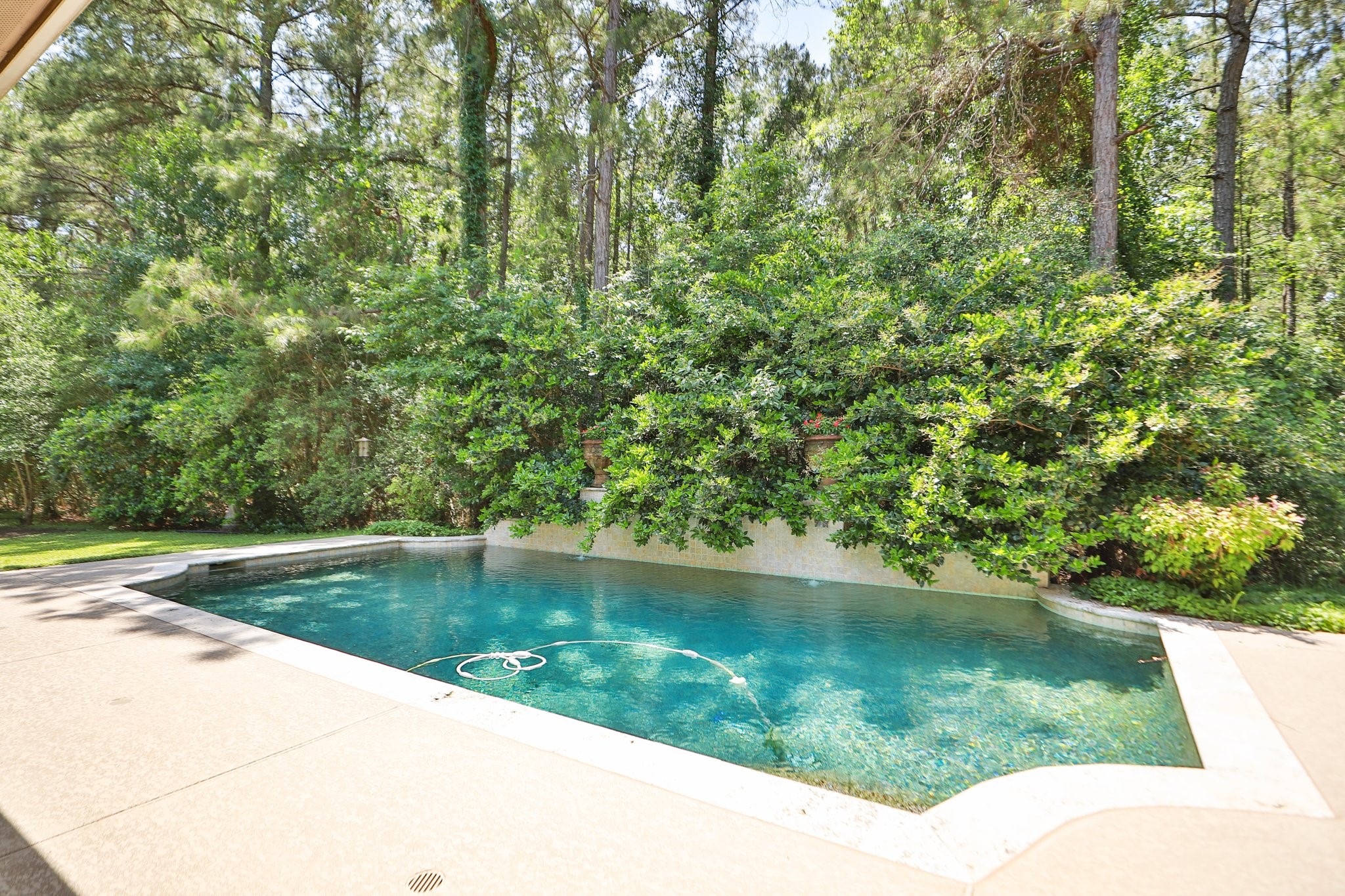7514 Saddle Blanket Drive Waller, TX 77484 - Photo 33 of 50 This photo features a serene backyard with a pool surrounded by lush greenery and tall trees, offering a private and tranquil setting. The pool area is bordered by a Sundek surface and has a pebble tech finish. Perfect place for relaxation and your outdoor enjoyment.