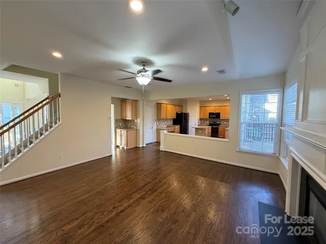 a view of an empty room with wooden floor and a kitchen