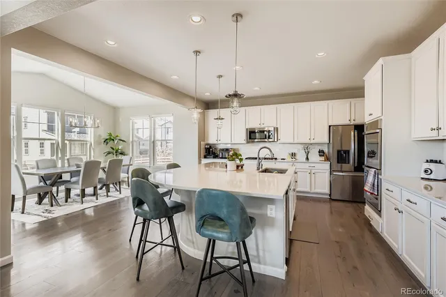 a kitchen with stainless steel appliances kitchen island granite countertop a stove a refrigerator a kitchen island a dining table and chairs with wooden floor