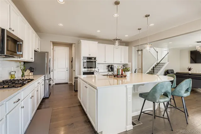 a kitchen with stainless steel appliances kitchen island granite countertop a stove top oven a sink a refrigerator white cabinets and wooden floor