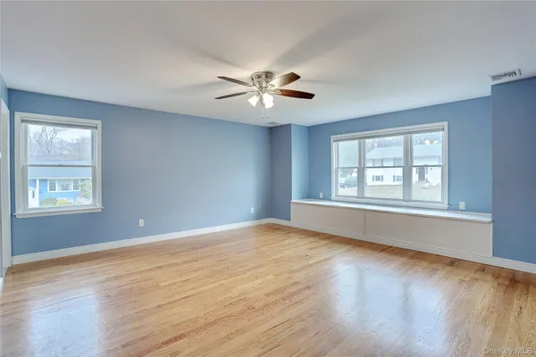 a view of an empty room with chandelier fan and wooden floor