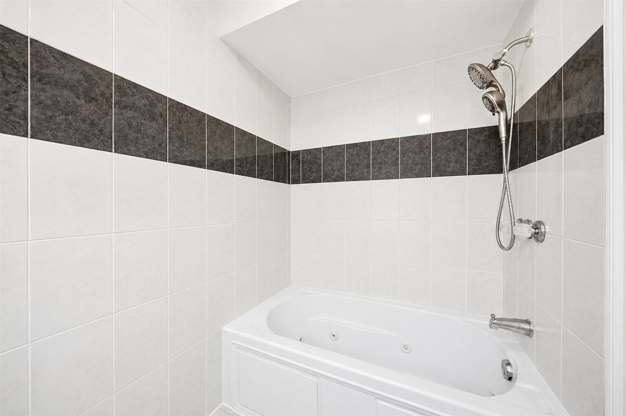 15414 Ripplestream Drive Houston, TX 77068 - Photo 24 of 41 Primary bath features a relaxing jetted soaking tub and shower combo with clean white tile walls, a bold dark accent border, and a multi functional showerhead and matching hardware.