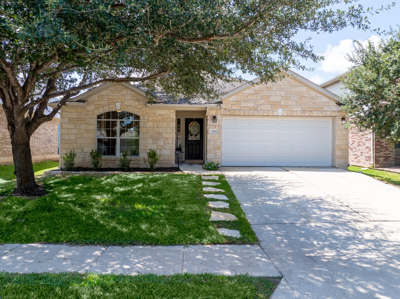 1391 Stone Rim Loop Buda, TX 78610 - Photo 28 of 35 A charming single-story residence boasts an inviting stone facade, a well-kept lawn, and a welcoming entry.