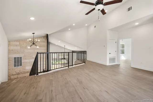 an empty room with wooden floor chandelier fan and windows