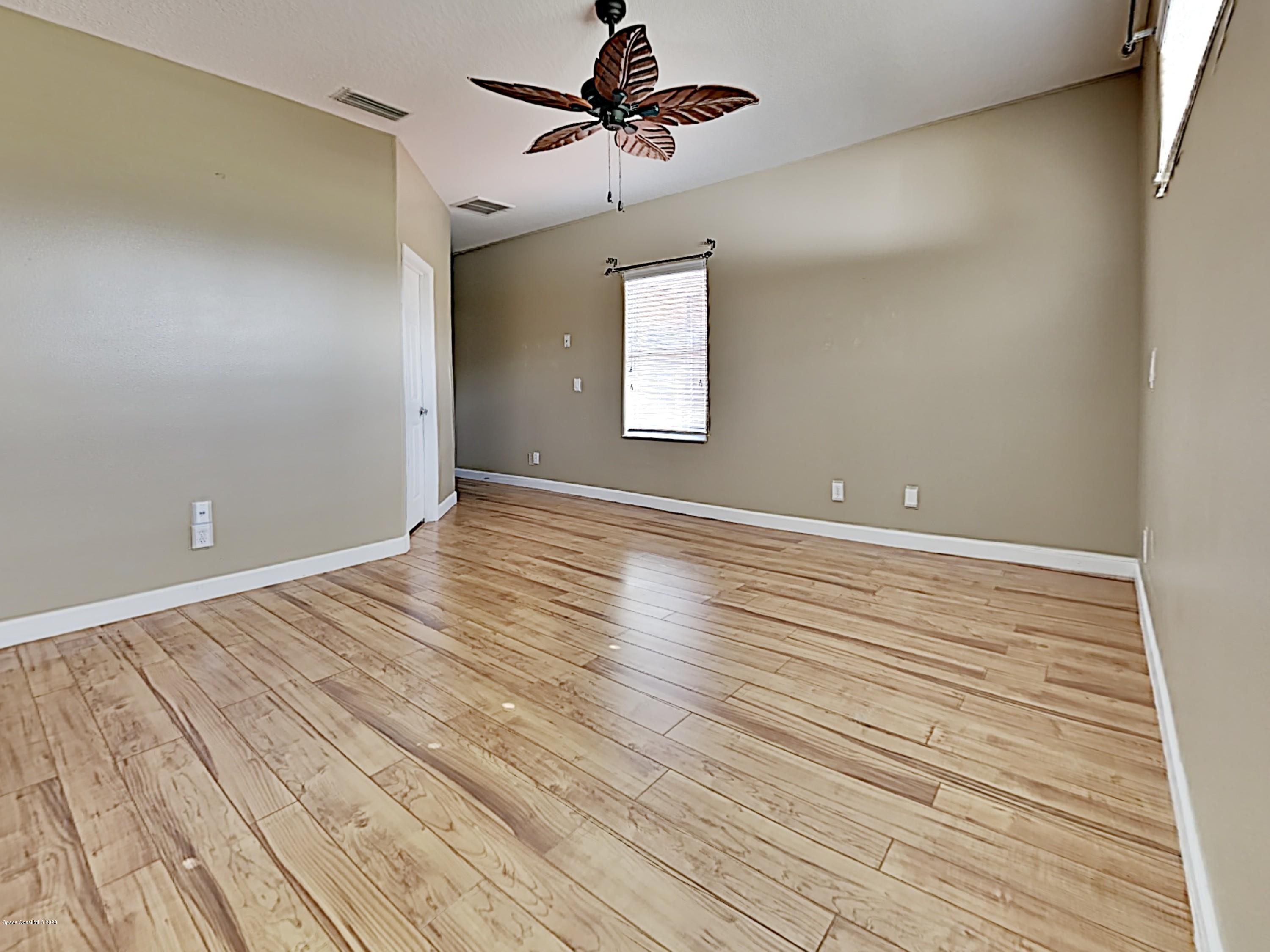 830 Riviera Drive Northeast Palm Bay, FL 32905 - Photo 10 of 21 an empty room with wooden floor chandelier fan and windows