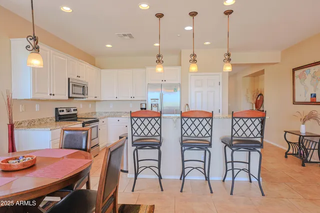 a kitchen with stainless steel appliances kitchen island granite countertop a dining table chairs and white cabinets