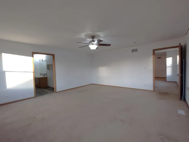 an empty room with chandelier fan and windows