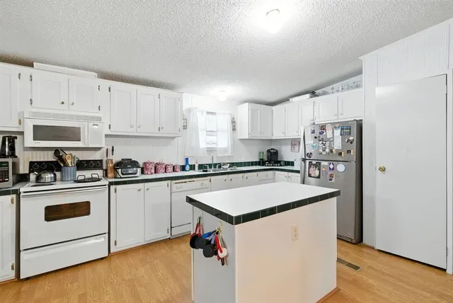 a kitchen with refrigerator a stove a sink dishwasher and white cabinets with wooden floor