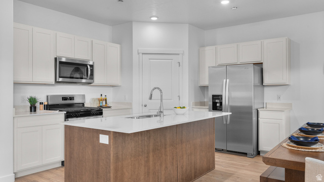 2032 East Dorset Way, Unit 286 Salem, UT 84653 - Photo 8 of 23 Modern kitchen featuring a central island with an undermount sink, white shaker cabinetry, stainless steel appliances, light-toned countertops, and wood-finish flooring