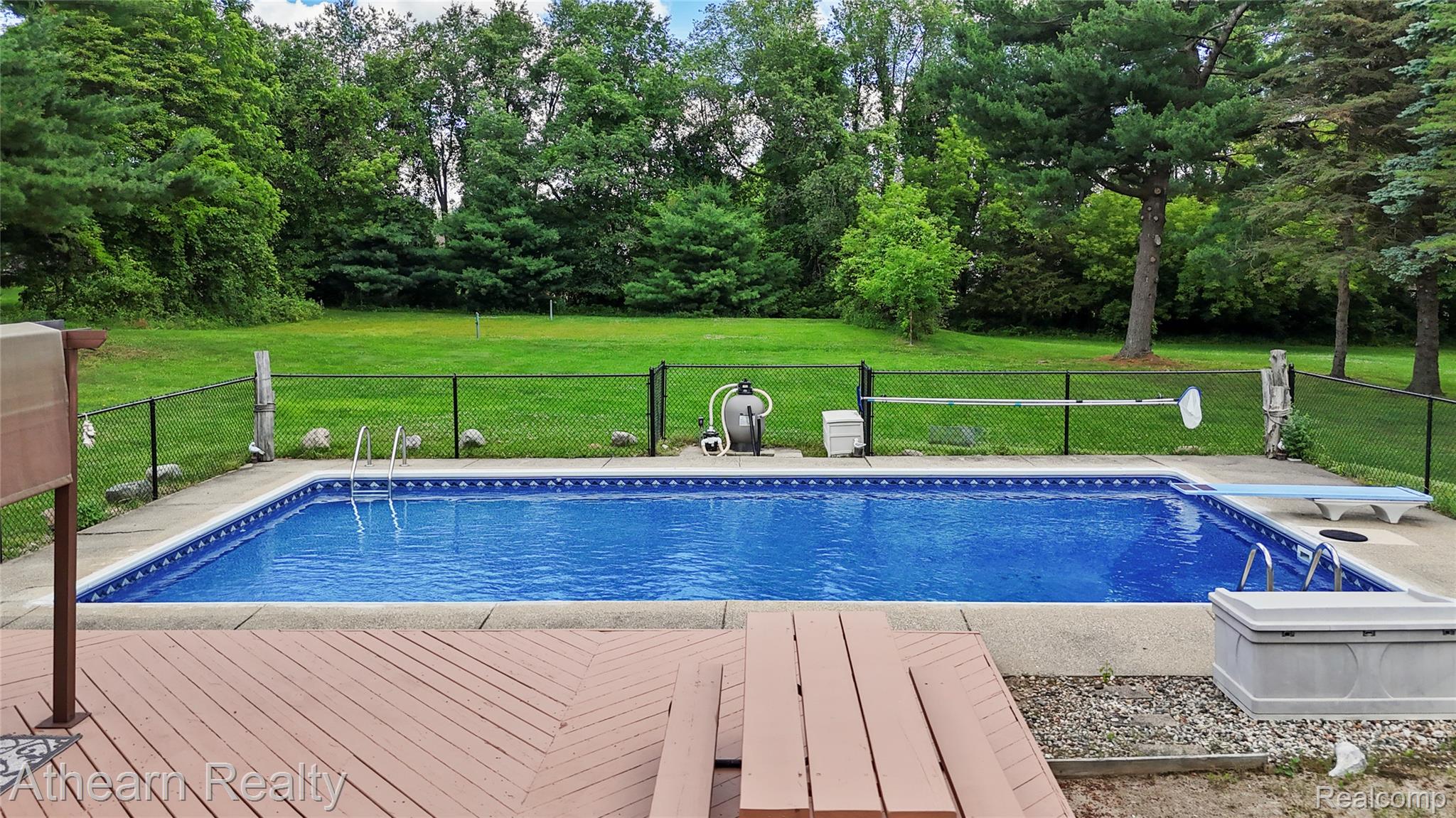 12427 Foley Road Fenton, MI 48430 - Photo 10 of 47 In-ground swimming pool with a diving board, surrounded by a concrete patio and a perimeter fence