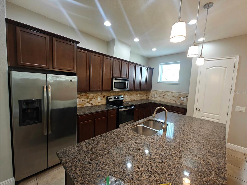 8075 Schelling Street Orlando, FL 32827 - Photo 3 of 51 a kitchen with granite countertop stainless steel appliances a refrigerator a stove a sink cabinets and a dining table