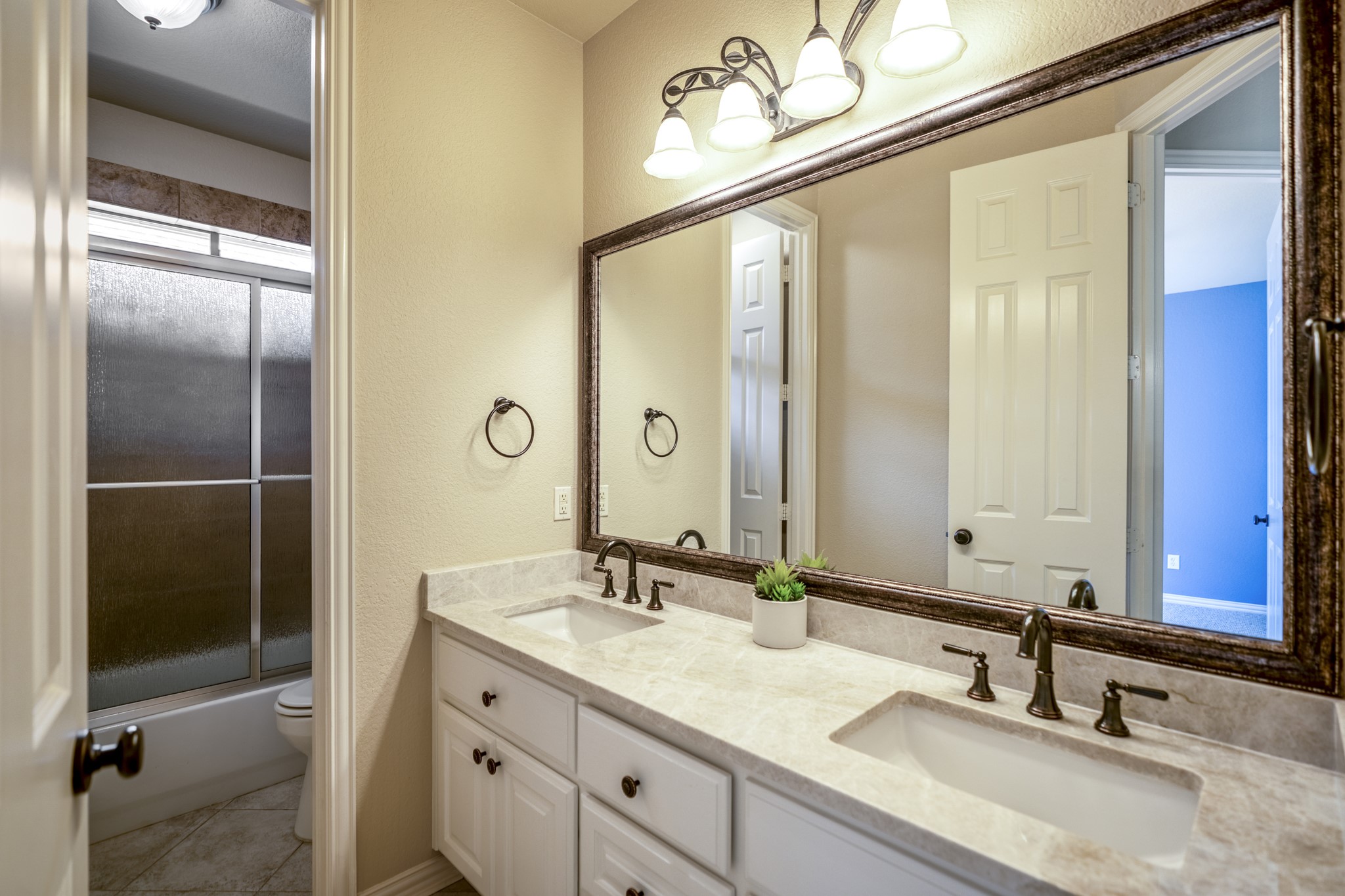 2407 Hendricks Lakes Drive Spring, TX 77388 - Photo 27 of 50 Connected to the second bedroom, this bath continues the suite feel with a double vanity, framed mirrors, upgraded lighting, and a glass-enclosed shower. The doorway on the left leads back into the bedroom, keeping this front-of-home space private and convenient while still feeling polished and connected to the home’s custom finishes.