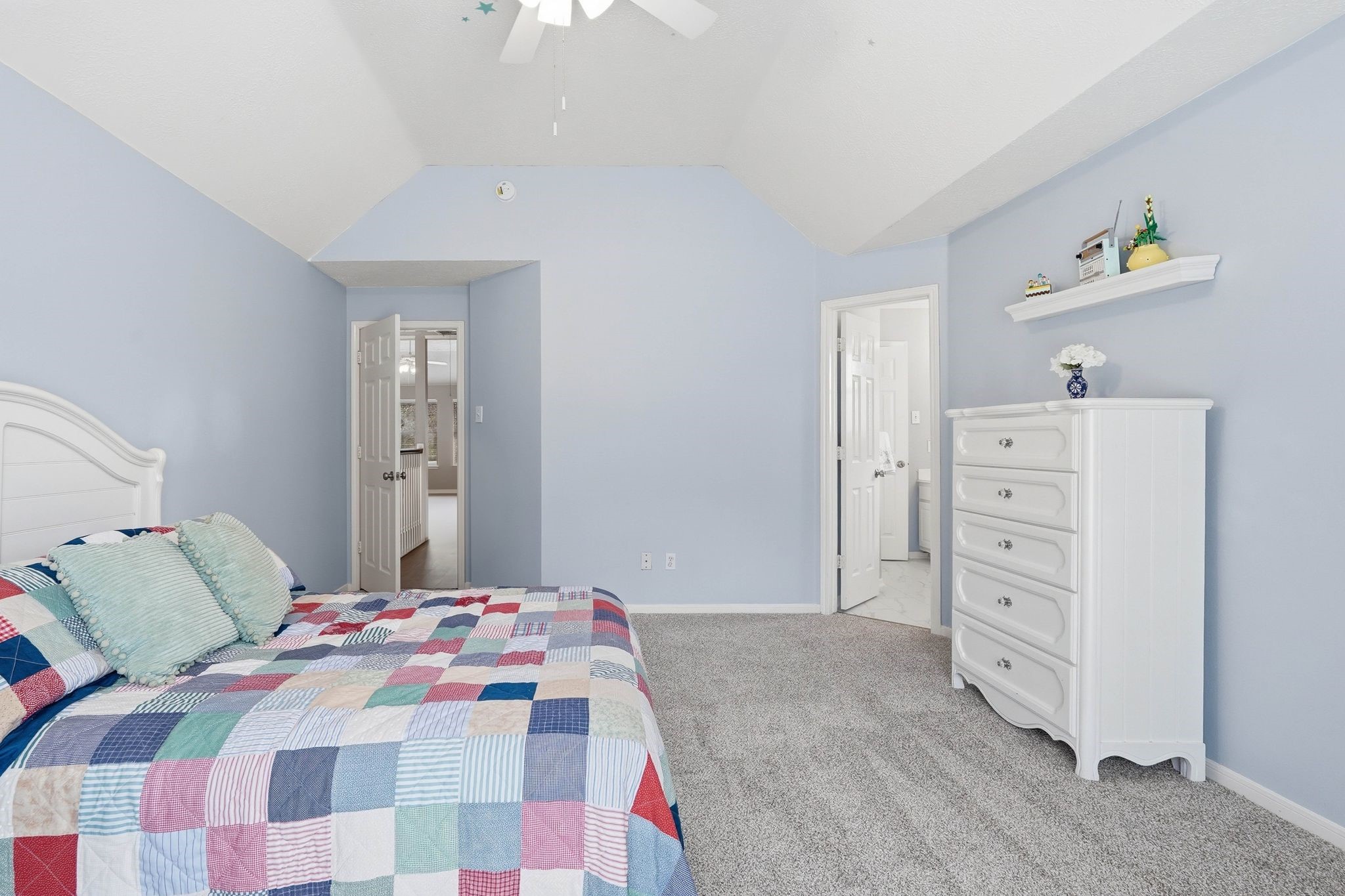 2515 Woodsboro Drive Spring, TX 77388 - Photo 31 of 44 The photo shows a cozy bedroom with soft blue walls and a vaulted ceiling. There's an en-suite bathroom and a doorway leading to another room, enhancing convenience and accessibility.