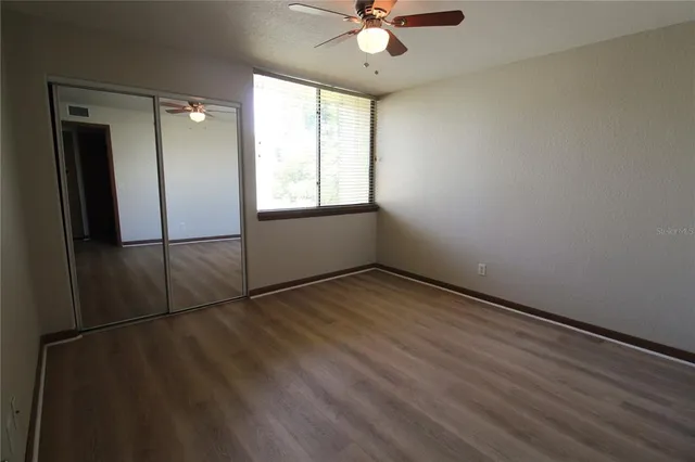 an empty room with wooden floor fan and windows