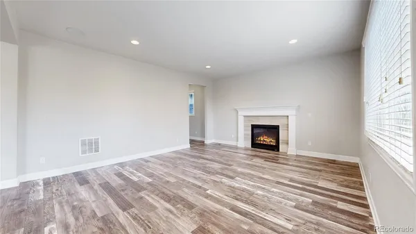 a view of an empty room with wooden floor fireplace and a window