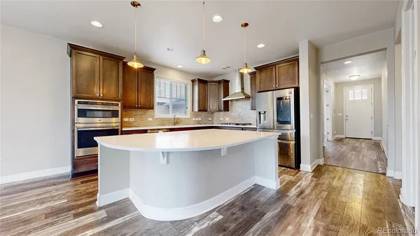 a kitchen with kitchen island granite countertop a refrigerator oven a sink dishwasher and cabinets with wooden floor