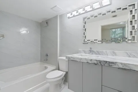 a bathroom with a granite countertop sink a mirror a toilet and bathtub