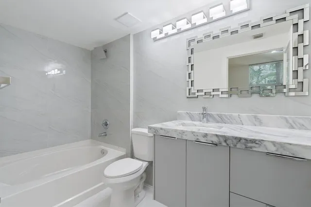a bathroom with a granite countertop sink a mirror a toilet and bathtub