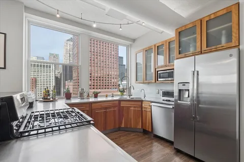 a kitchen with stainless steel appliances granite countertop a stove a sink dishwasher a refrigerator and white cabinets with wooden floor