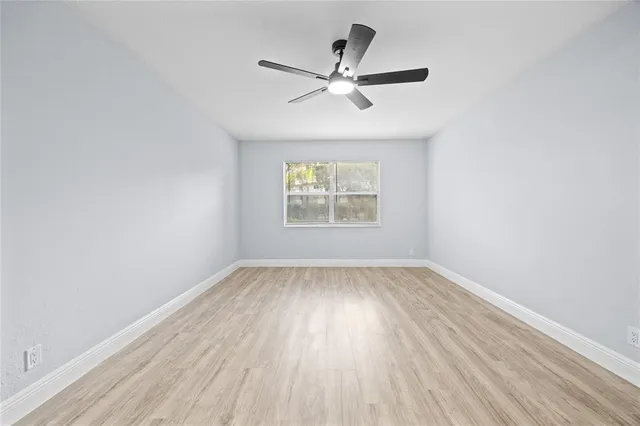 an empty room with wooden floor window and ceiling fan