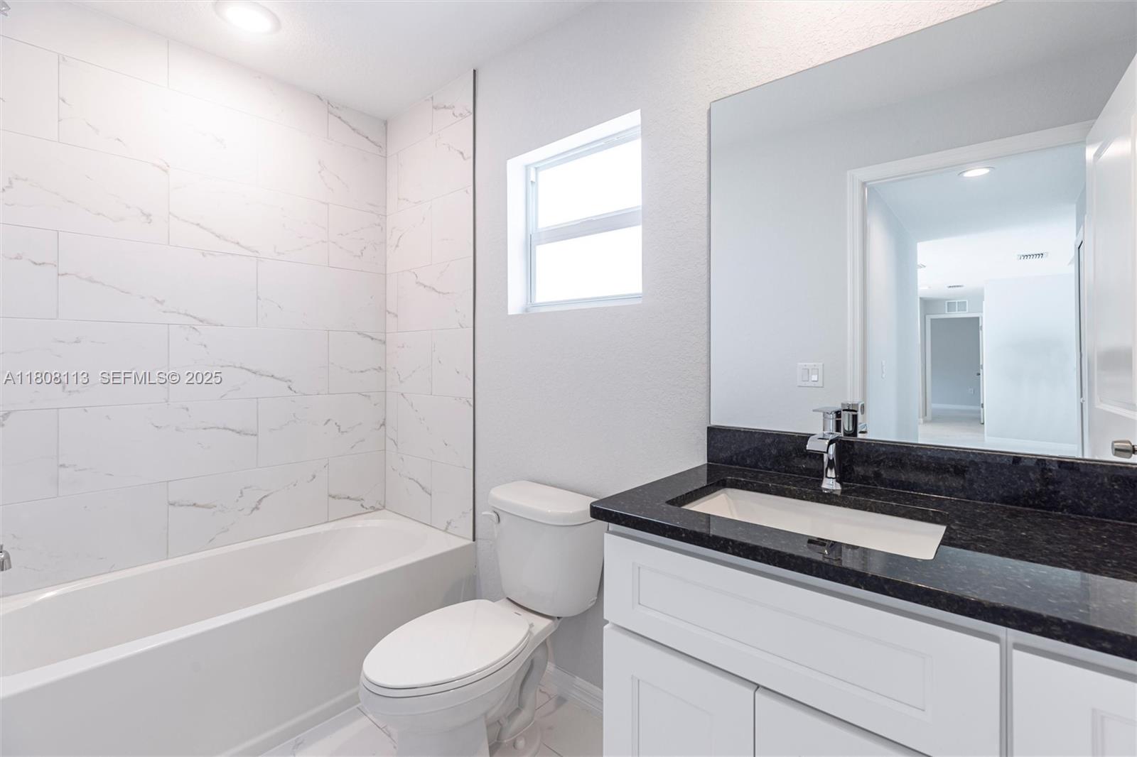 2006 Rosa Court, Unit 2006 Lehigh Acres, FL 33972 - Photo 13 of 22 a bathroom with a granite countertop sink a toilet a mirror a bathtub and shower