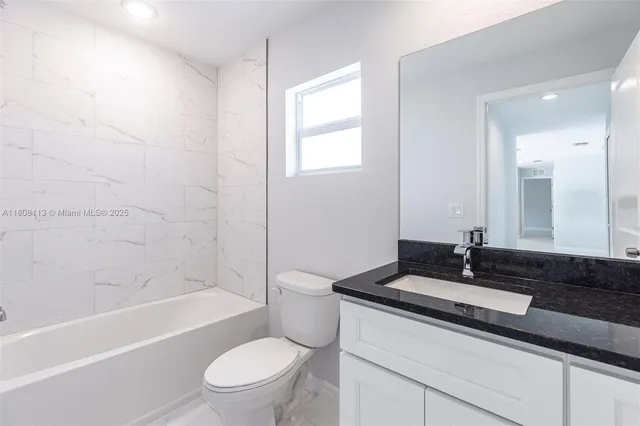 a bathroom with a granite countertop sink a toilet a mirror a bathtub and shower