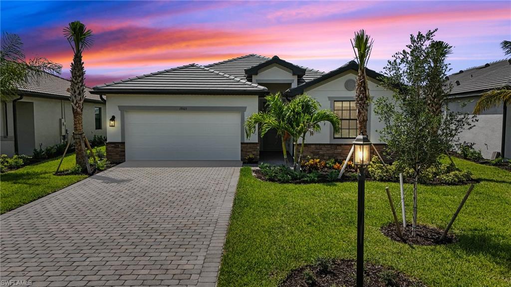 19105 Hinkley Drive Estero, FL 33928 - Photo 2 of 48 Ranch-style house featuring decorative driveway, an attached garage, stucco siding, and a yard