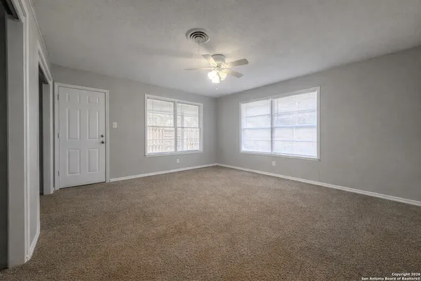 an empty room with chandelier fan and windows
