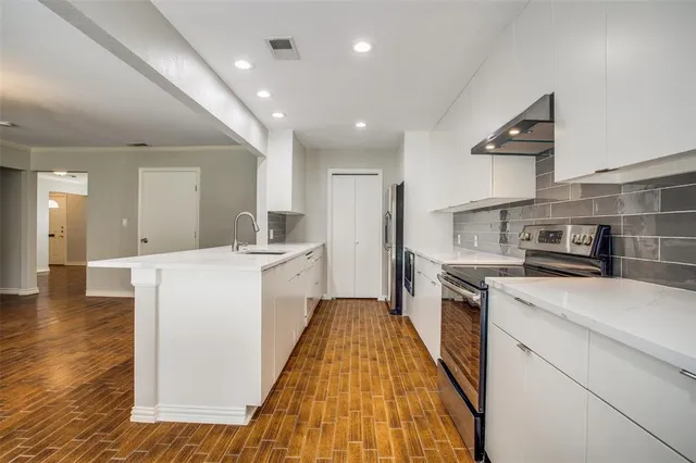 a kitchen with a sink a stove top oven and white wooden cabinets