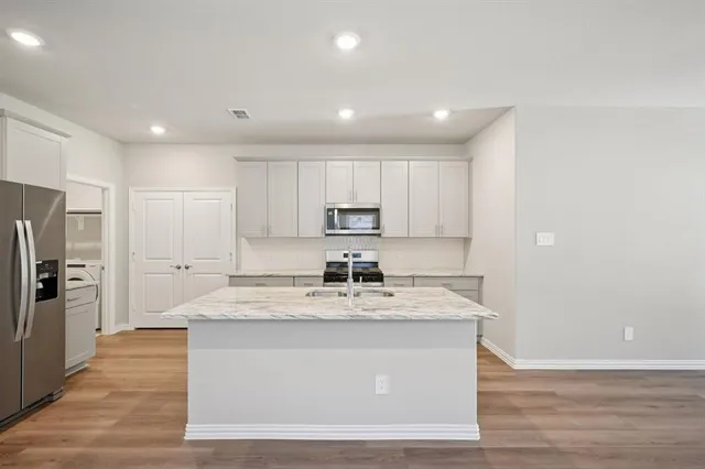 a large kitchen with stainless steel appliances granite countertop a sink dishwasher a refrigerator and a oven with wooden floor