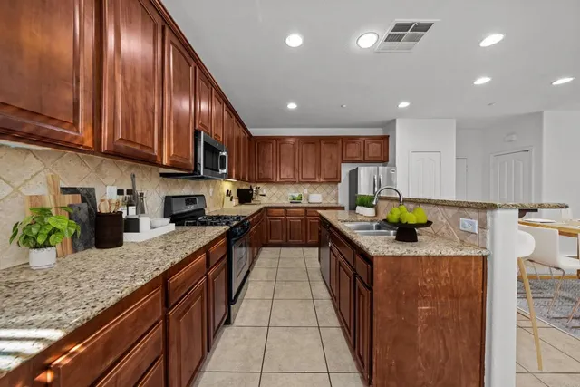 a kitchen with stainless steel appliances granite countertop wooden cabinets a sink a stove and a wooden floors