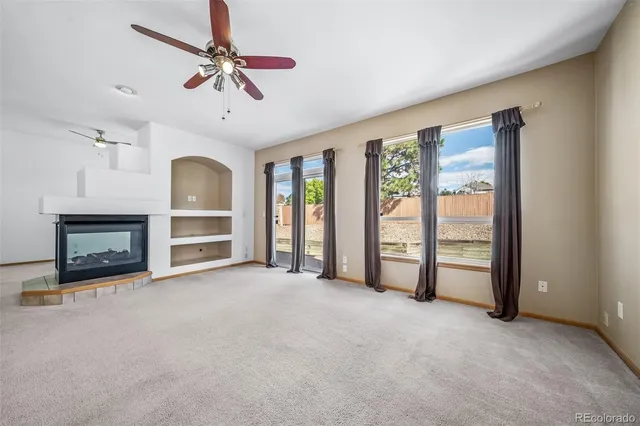 an empty room with windows fireplace and a ceiling fan
