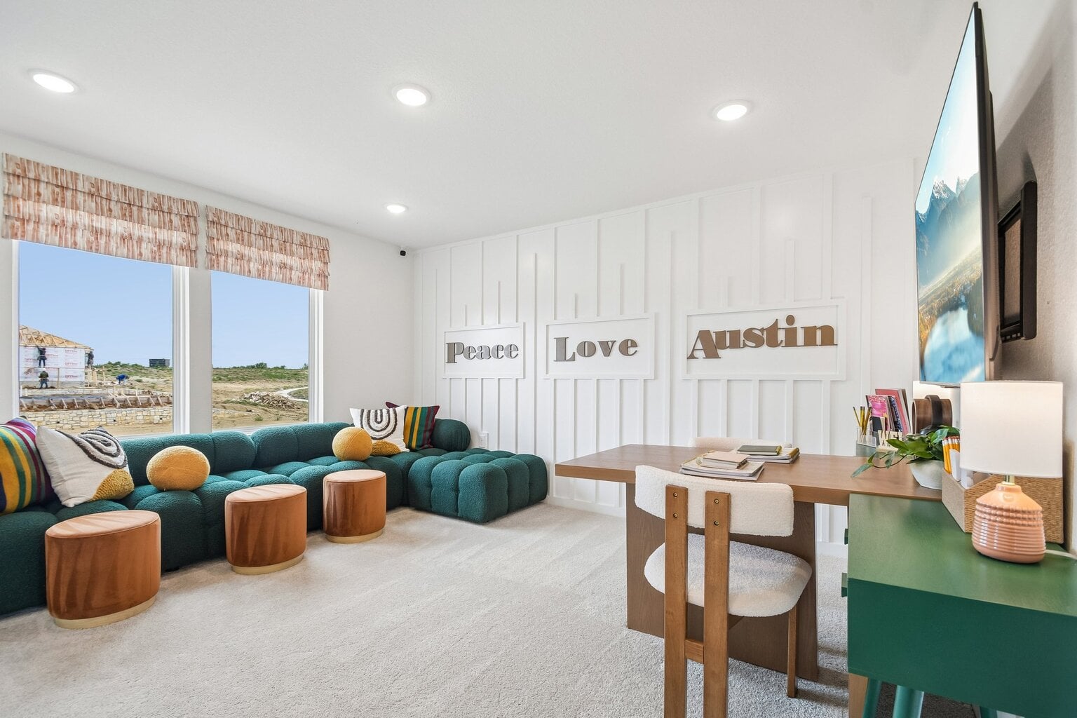10609 Trifecta Way Buda, TX 78610 - Photo 4 of 17 Recessed lighting illuminates this versatile living space, featuring a cozy corner sofa and a dedicated workspace, all set against a clean, paneled accent wall.