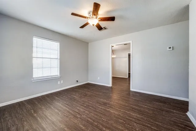 an empty room with wooden floor ceiling fan and windows