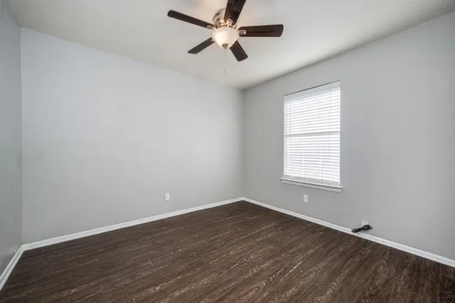 an empty room with wooden floor ceiling fan and windows