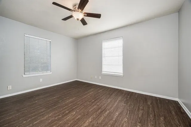 an empty room with wooden floor ceiling fan and windows
