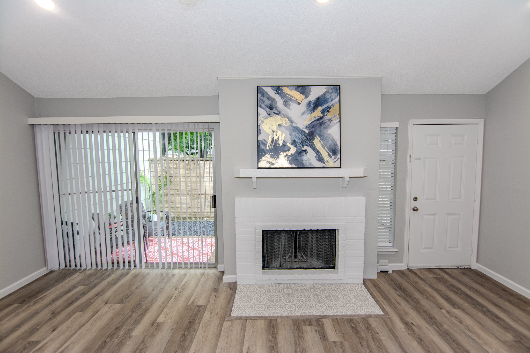 13009 Wirevine Lane Houston, TX 77072 - Photo 8 of 18 This cozy living room features a modern fireplace with a stylish mantel, contemporary artwork, and sliding glass doors leading to a patio. The space is bright with natural light and has sleek, Vinyl Plank wood-style flooring.