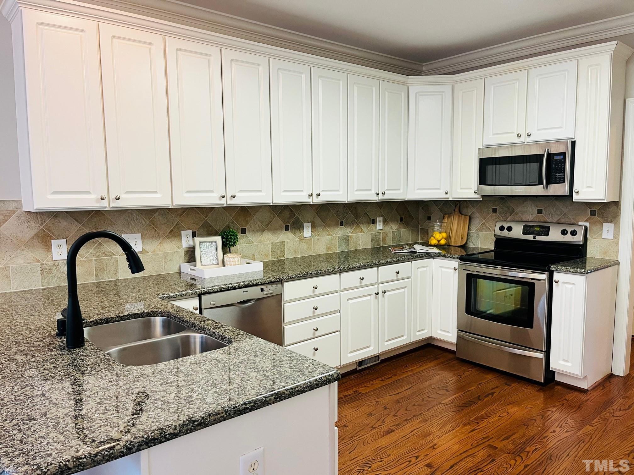 6317 Belle Crest Drive Raleigh, NC 27612 - Photo 3 of 29 a kitchen with granite countertop white cabinets and white appliances