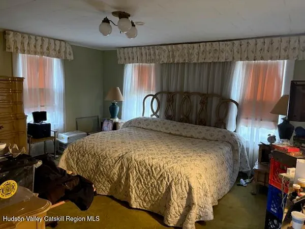 a bed sitting in a bedroom next to a window with pc on the table and a flat screen tv