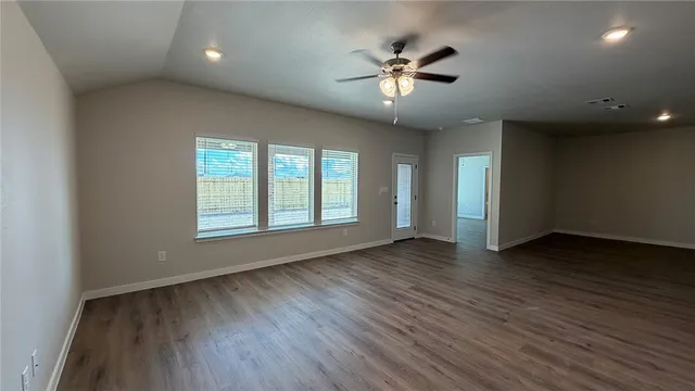 an empty room with wooden floor chandelier fan and windows