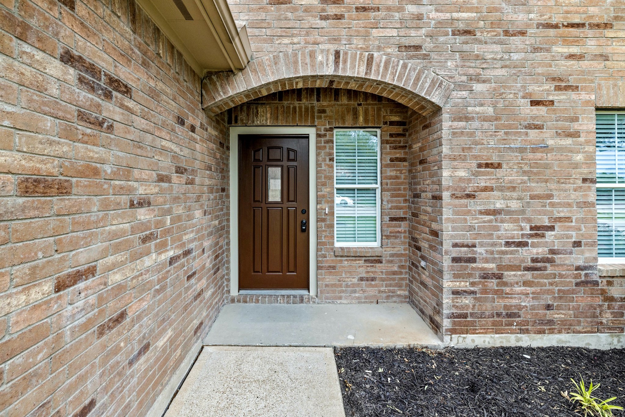 403 Red Hawk Drive Leander, TX 78641 - Photo 4 of 37 Brick exterior featuring an arched entryway, a dark wood-finish front door, and a concrete pathway leading to the entrance