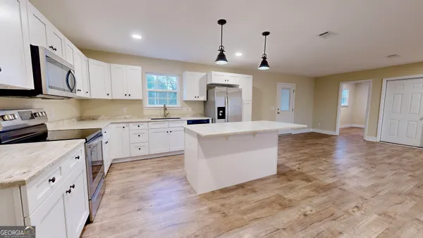 a large kitchen with stainless steel appliances granite countertop a stove a sink a refrigerator and white cabinets with wooden floor