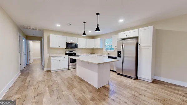 a kitchen with stainless steel appliances a refrigerator a sink dishwasher a stove and white cabinets with wooden floor
