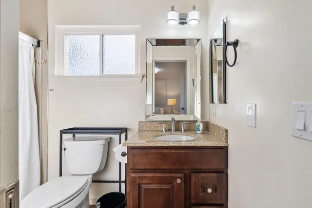 a bathroom with a granite countertop sink toilet and mirror