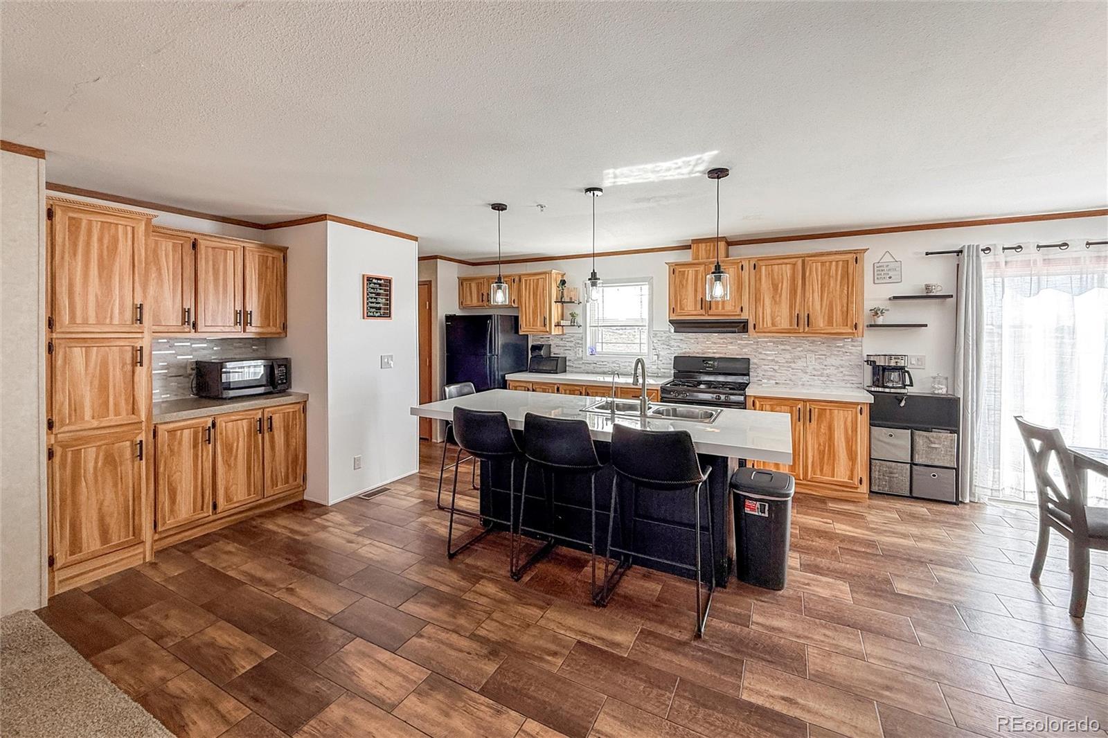 16412 Higgins Avenue Fort Lupton, CO 80621 - Photo 6 of 27 a kitchen with stainless steel appliances kitchen island granite countertop a refrigerator a stove a sink a dining table and chairs with wooden floor